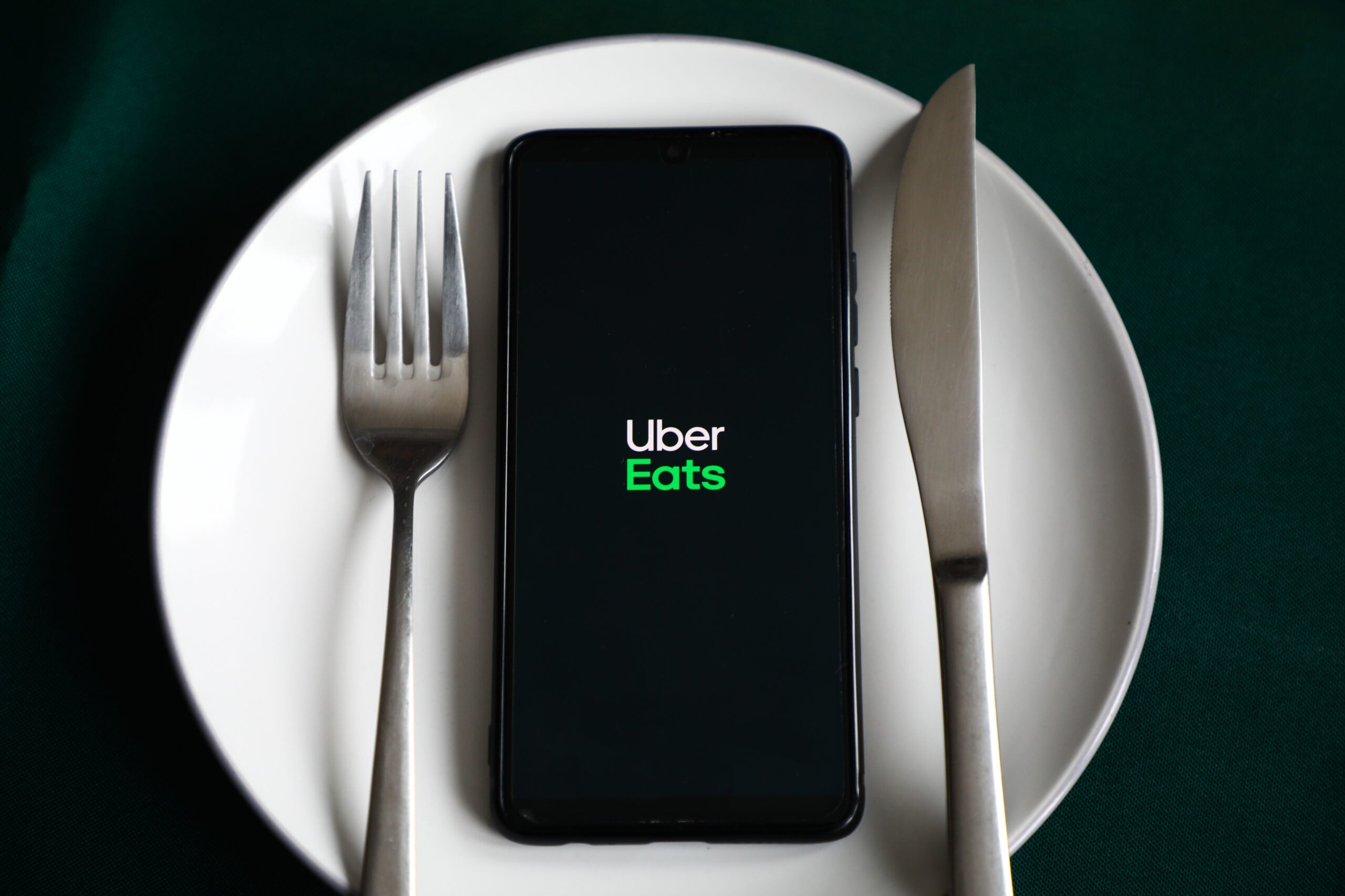 a phone showing Uber Eats sits on a white dinner plate between a fork and a knife