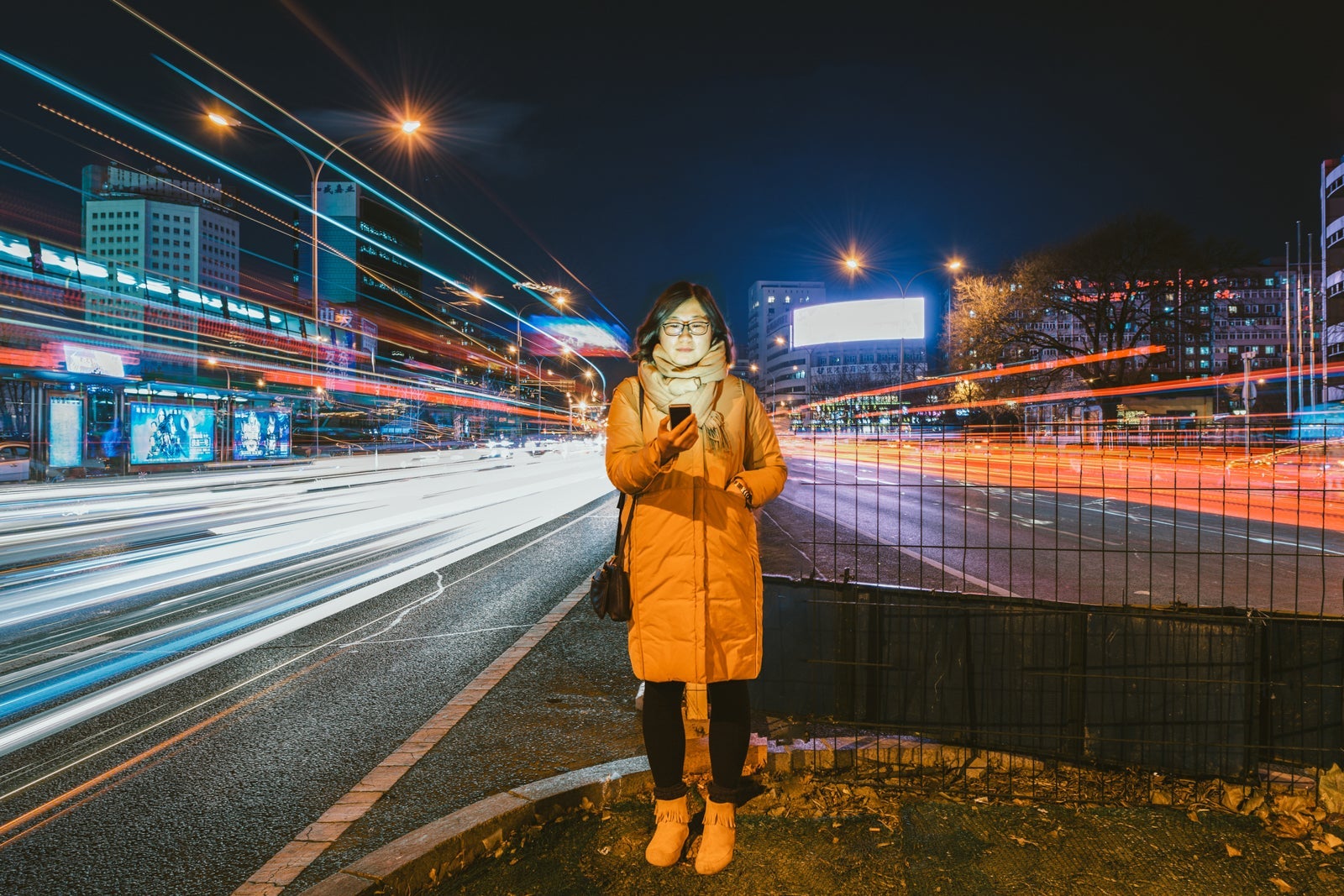 Young Asian Woman Using A Mobile Phone As Traffic Passes By