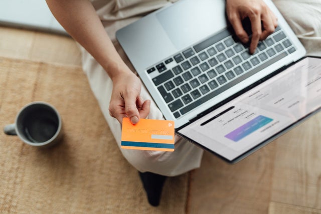 an unseen person holds a credit card while reading information on a laptop