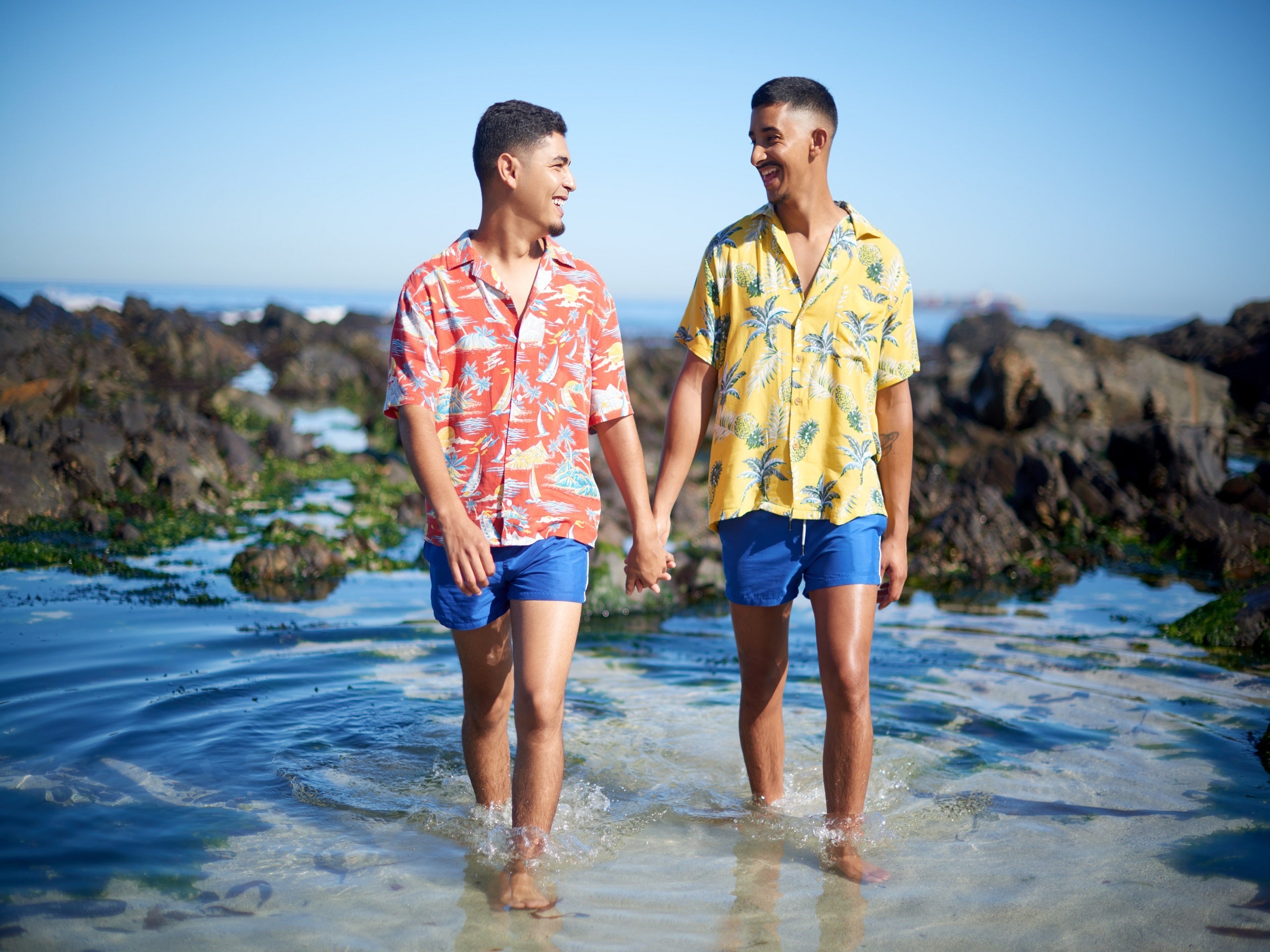 Two men in tropical shirts holding hands and walking on the beach