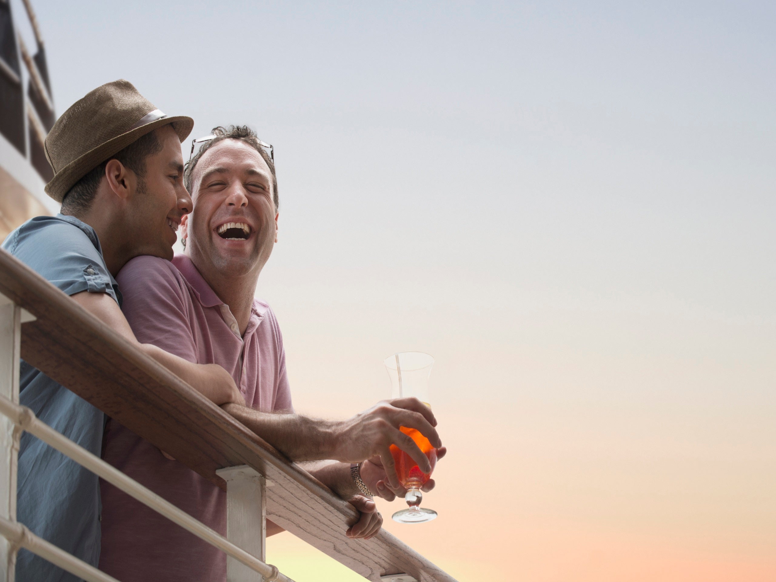 Two men cuddling with drinks along the railing of a cruise ship