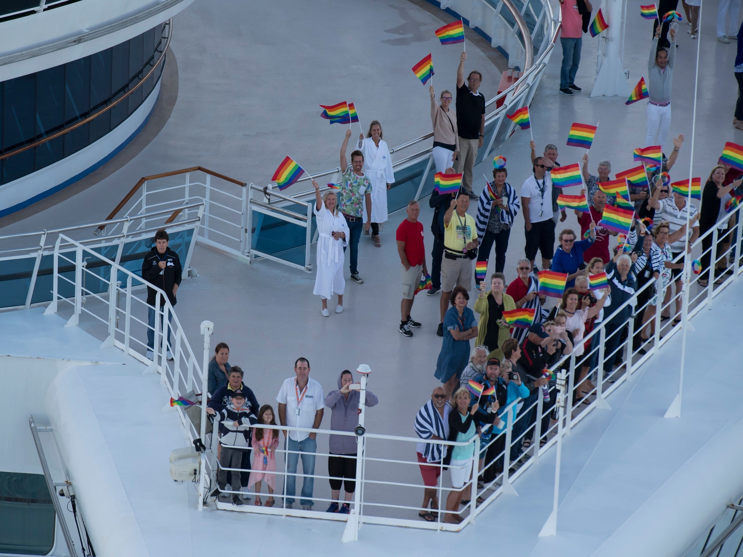 People standing against the railing on a cruis ship waving rainbow flags