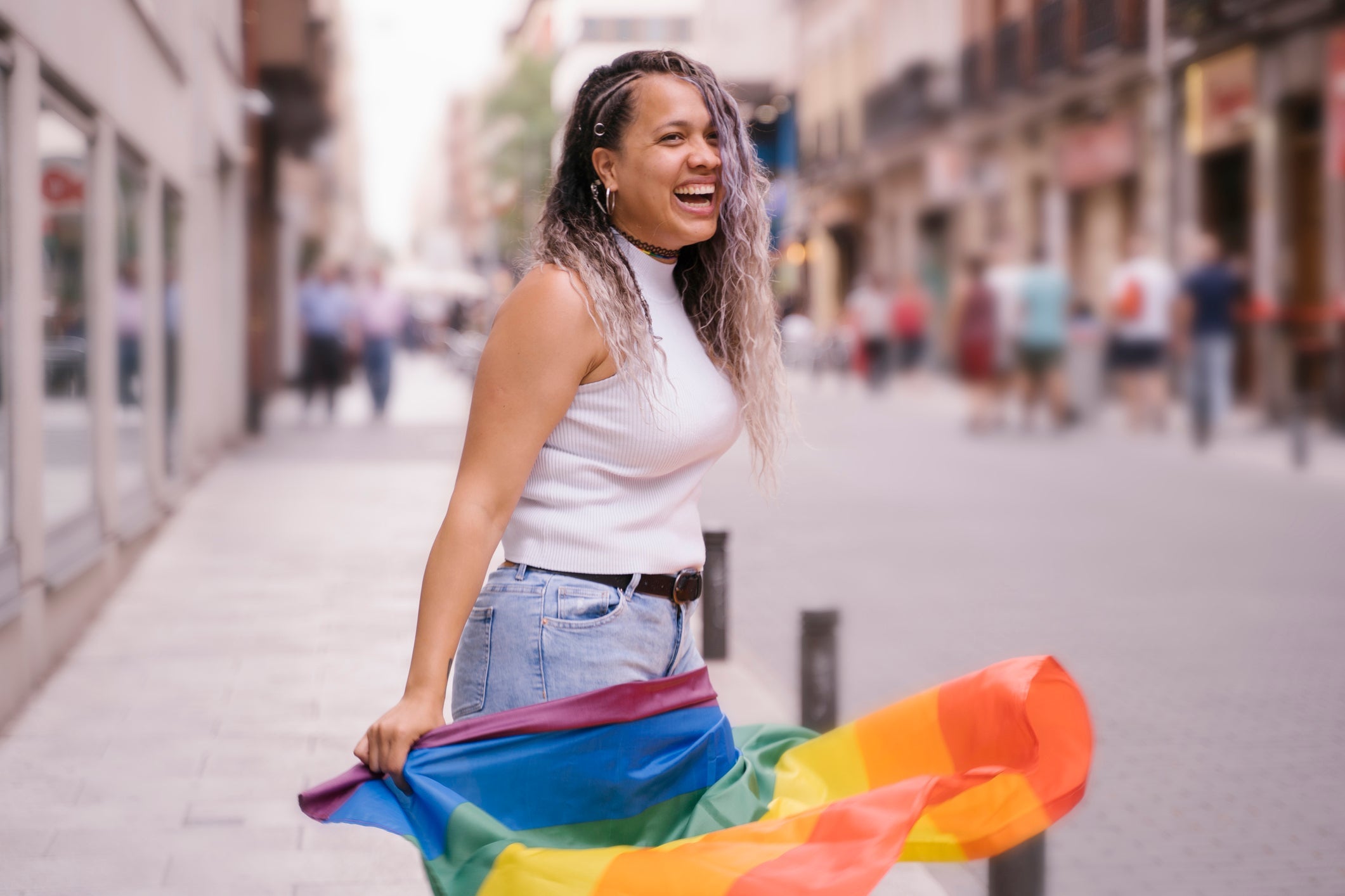 Smiling Young Woman With Rainbow Flag On Street In City