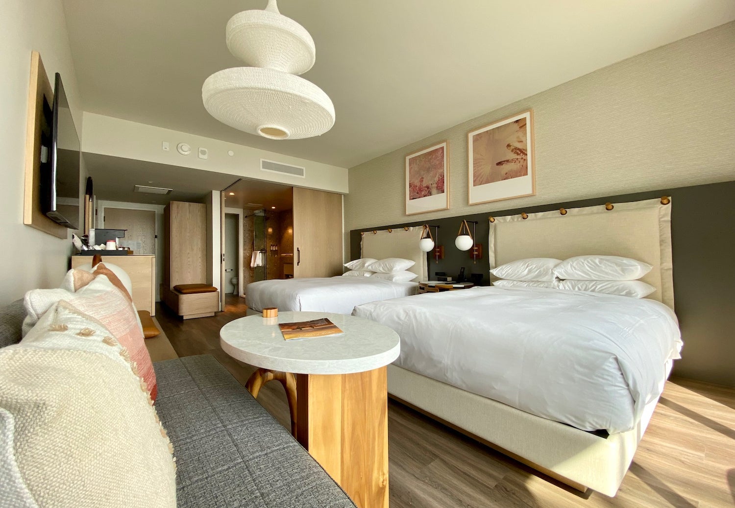 Hotel room with a seating area and table on one side, facing two queen beds