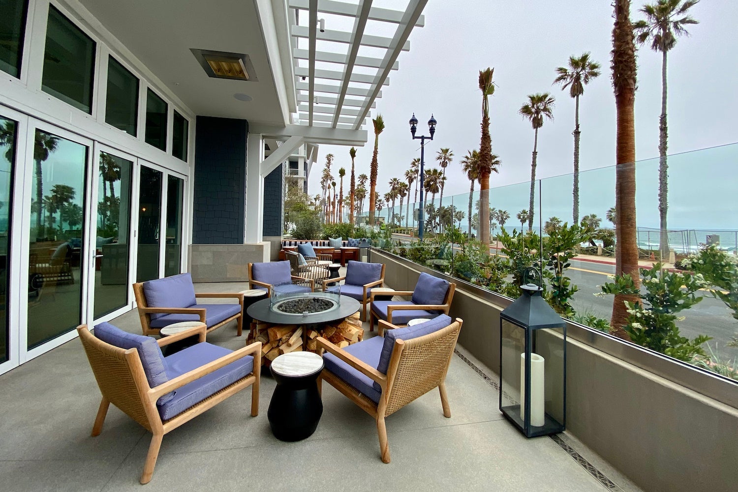 Hotel patio with seating and a firepit across from a tree-lined ocean pier