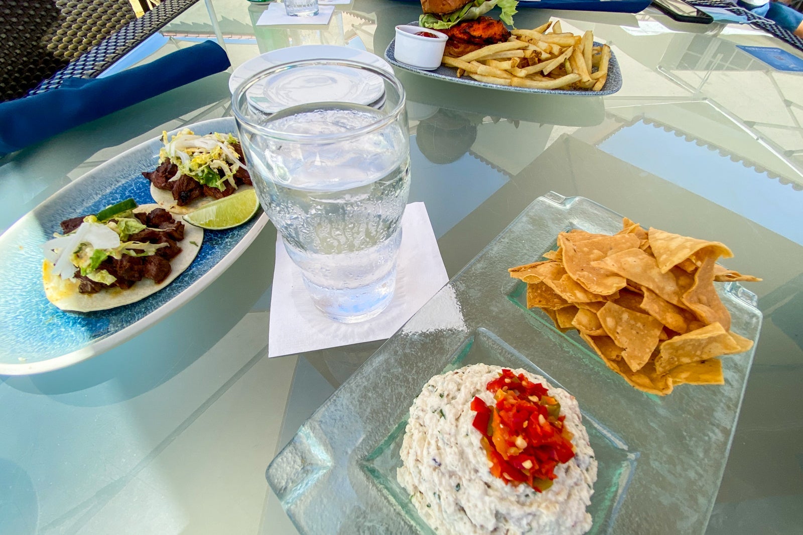 Table with a bowl of chips and dip, steak tacos and a burger with fries