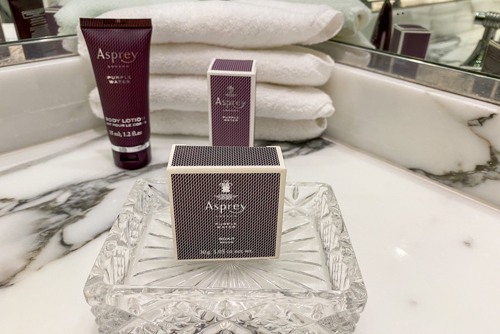 Asprey soap and lotion packets placed on a bathroom counter, with towels in the background