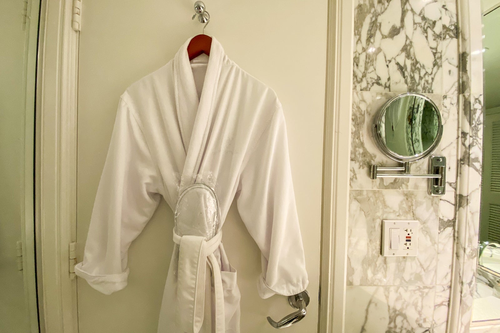White bathrobe and slippers hanging on a hotel bathroom door