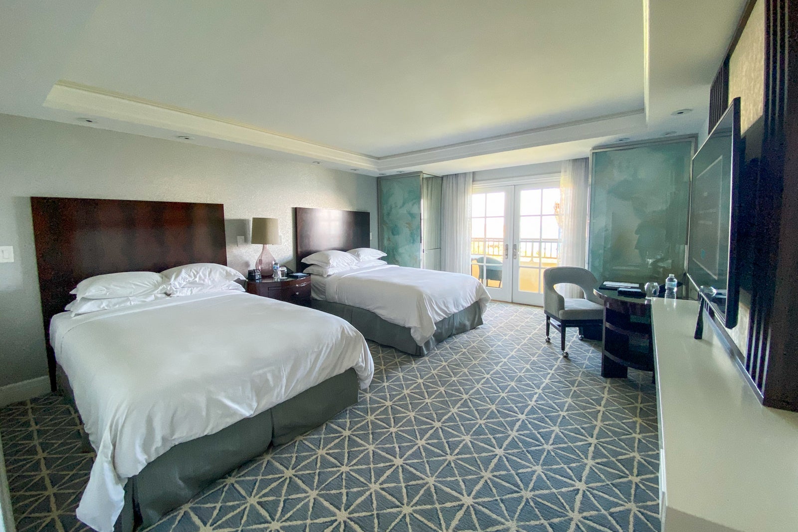 Two double beds facing a desk, with french doors leading to a balcony