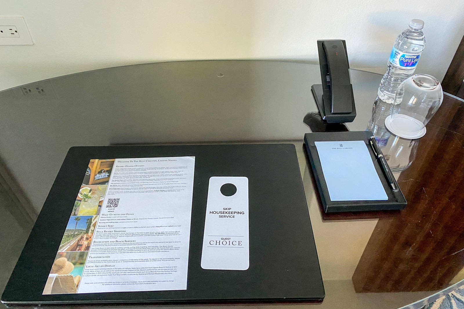 Hotel desk with an amenities menu, writing pad and telephone