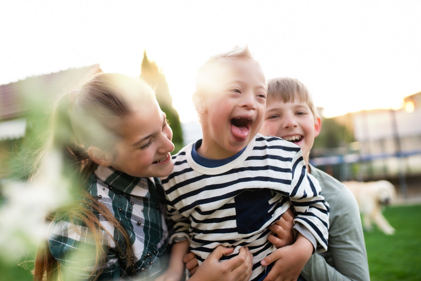 Three siblings playing outside with dog in the background.