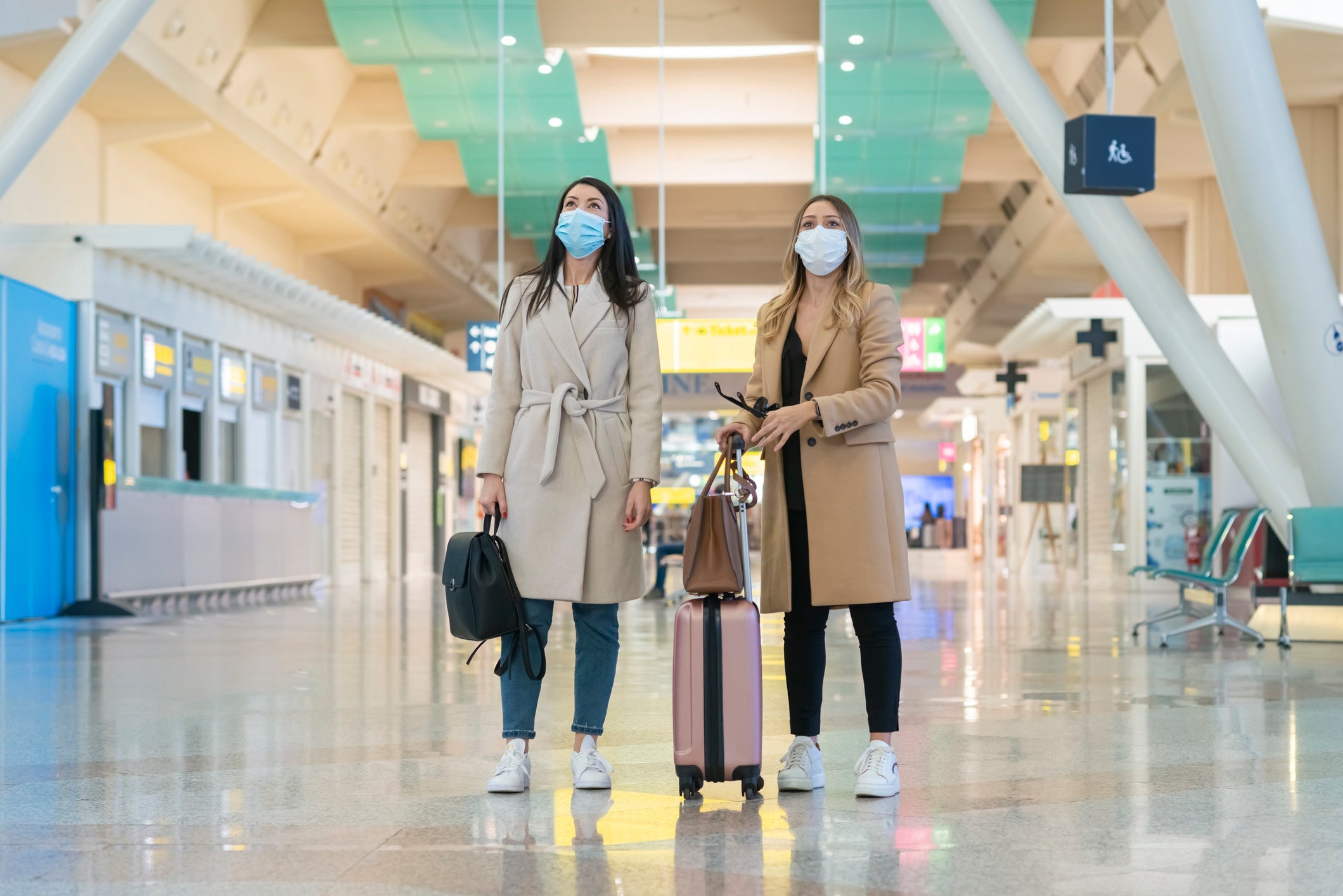 Two young women wearing masks while waiting together in an airport (Photo by Francesco Carta fotografo/Getty Images)