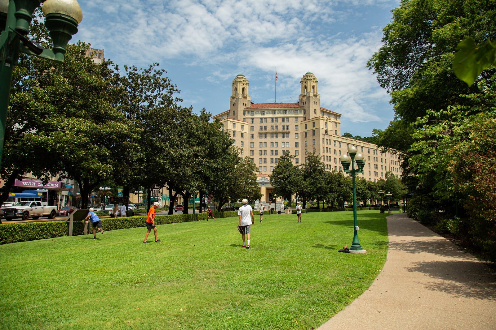 A group of boys practices throwing baseballs on the open lawn with a large two pillared hotel behind them.