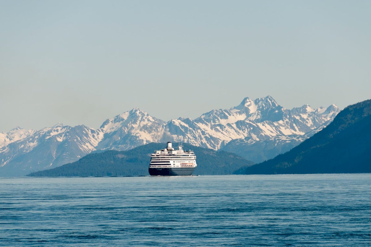 A cruise ship sails in the water with snow-capped mountains in the background