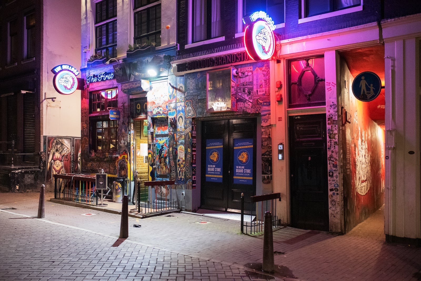 A nighttime view of a storefront containing a cannabis cafe with a sidewalk and streetlights out front