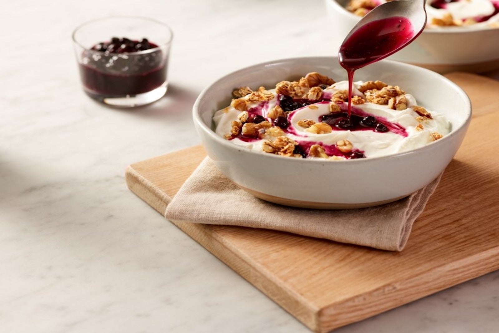 bowl of yogurt on wooden cutting board with spoon of berry compote pouring down