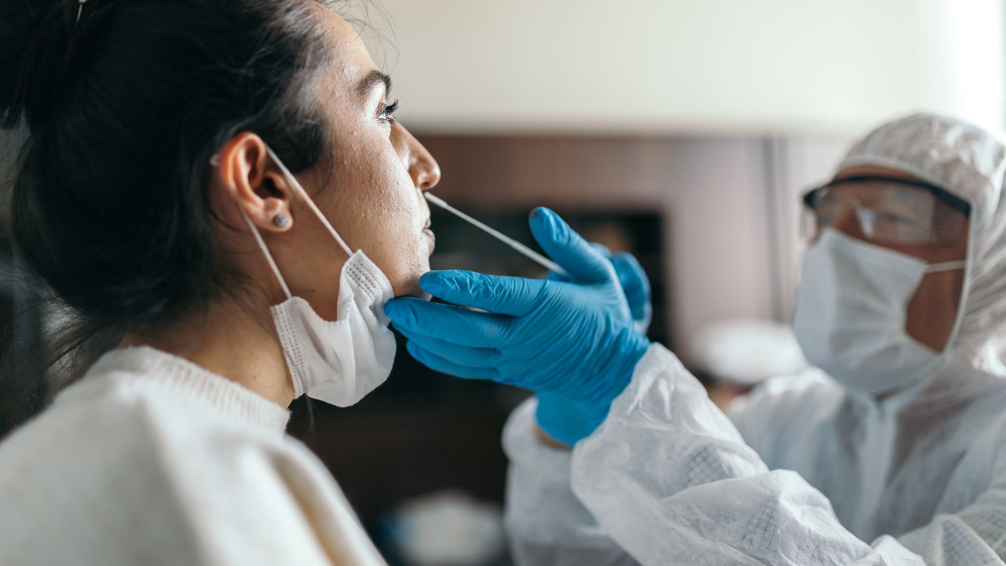 Doctor in protective workwear taking nose swab test from young woman