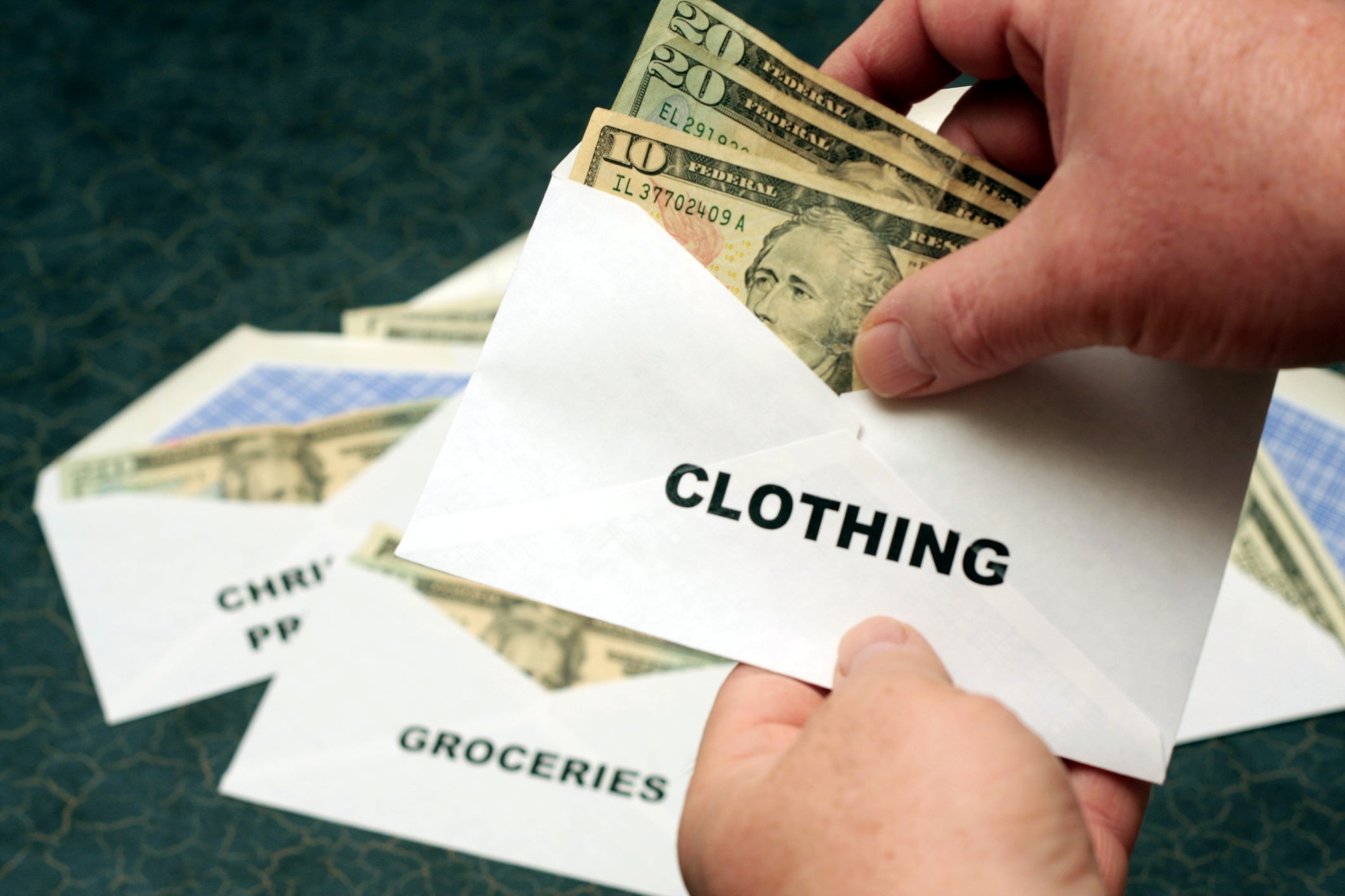 an unseen person holds envelopes labeled clothing, groceries and Christmas shopping, each with cash inside