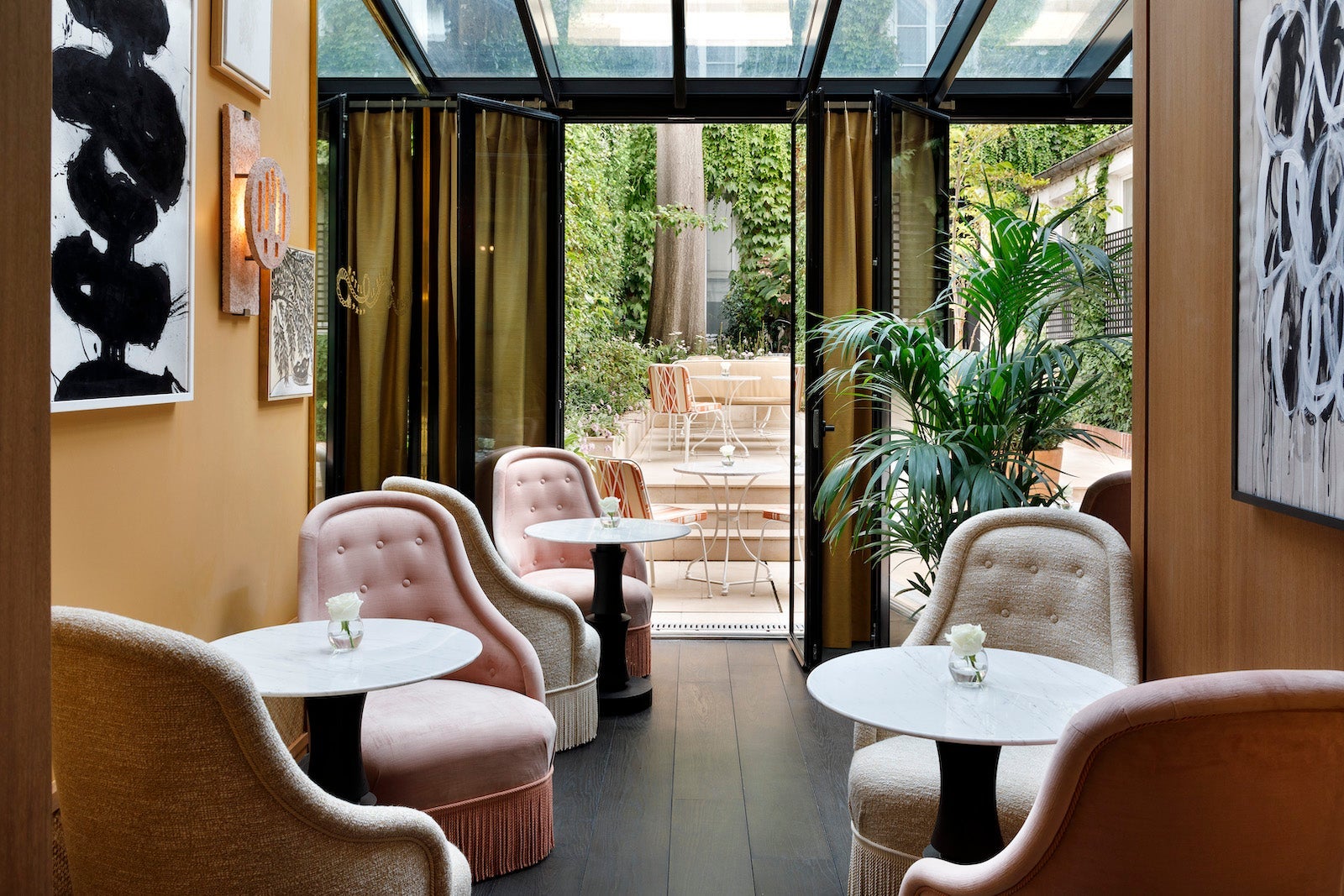 small lobby with pink, tufted chairs, black and white art, and open doors leading to a green terrace