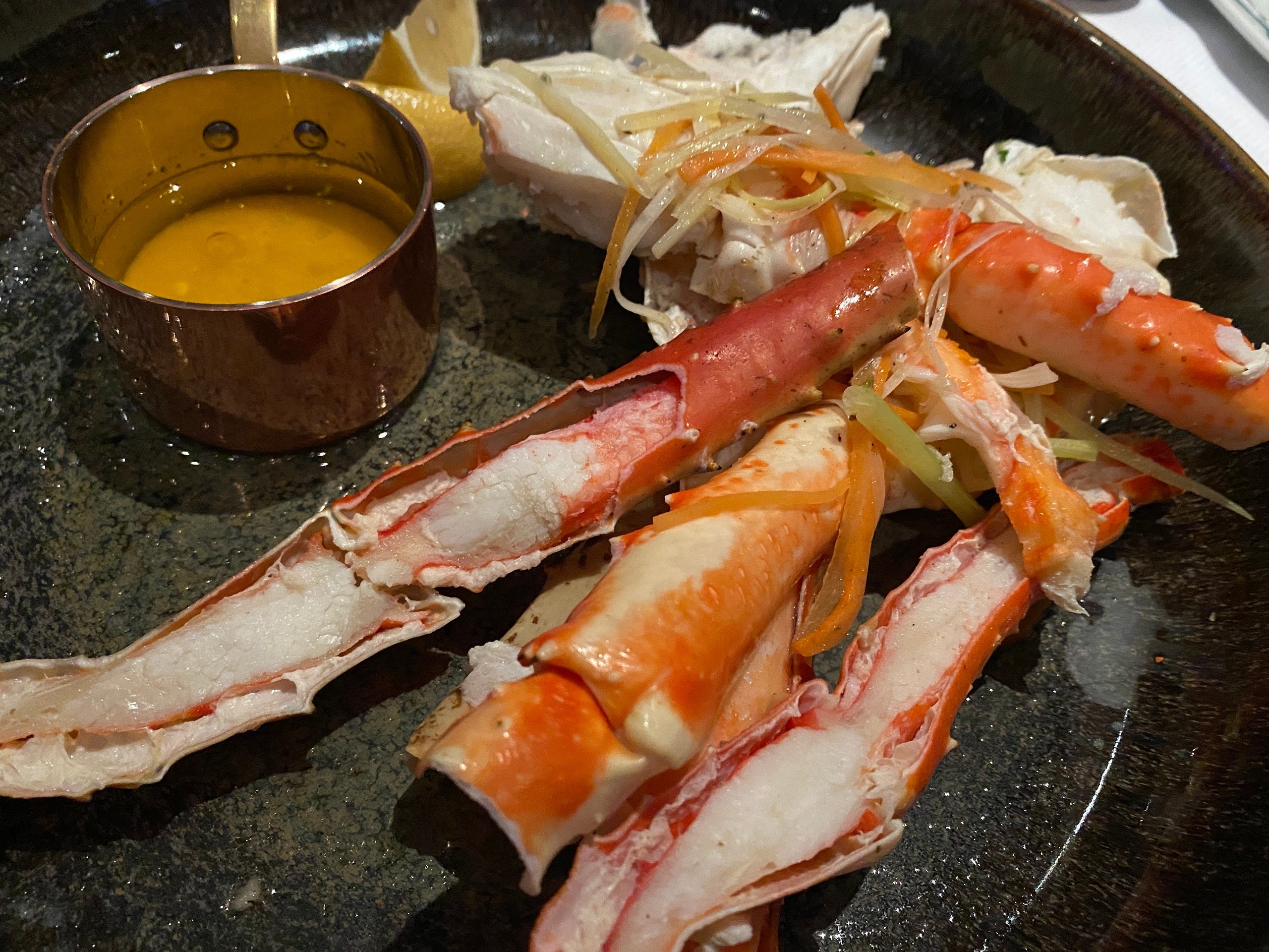 A plate of Alaskan crab legs sits on the table next to a cup of drawn butter.