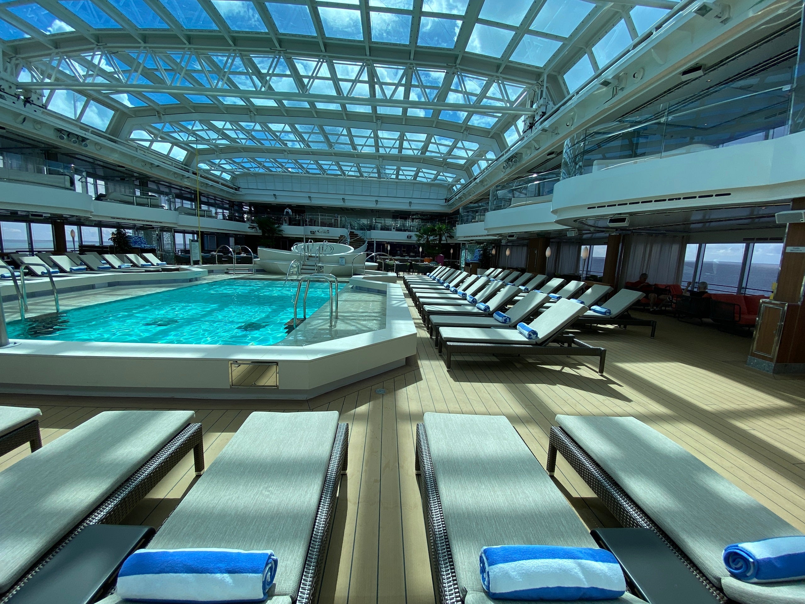 An elegant cruise ship pool surrounded by deck chairs and covered with a retractable glass roof