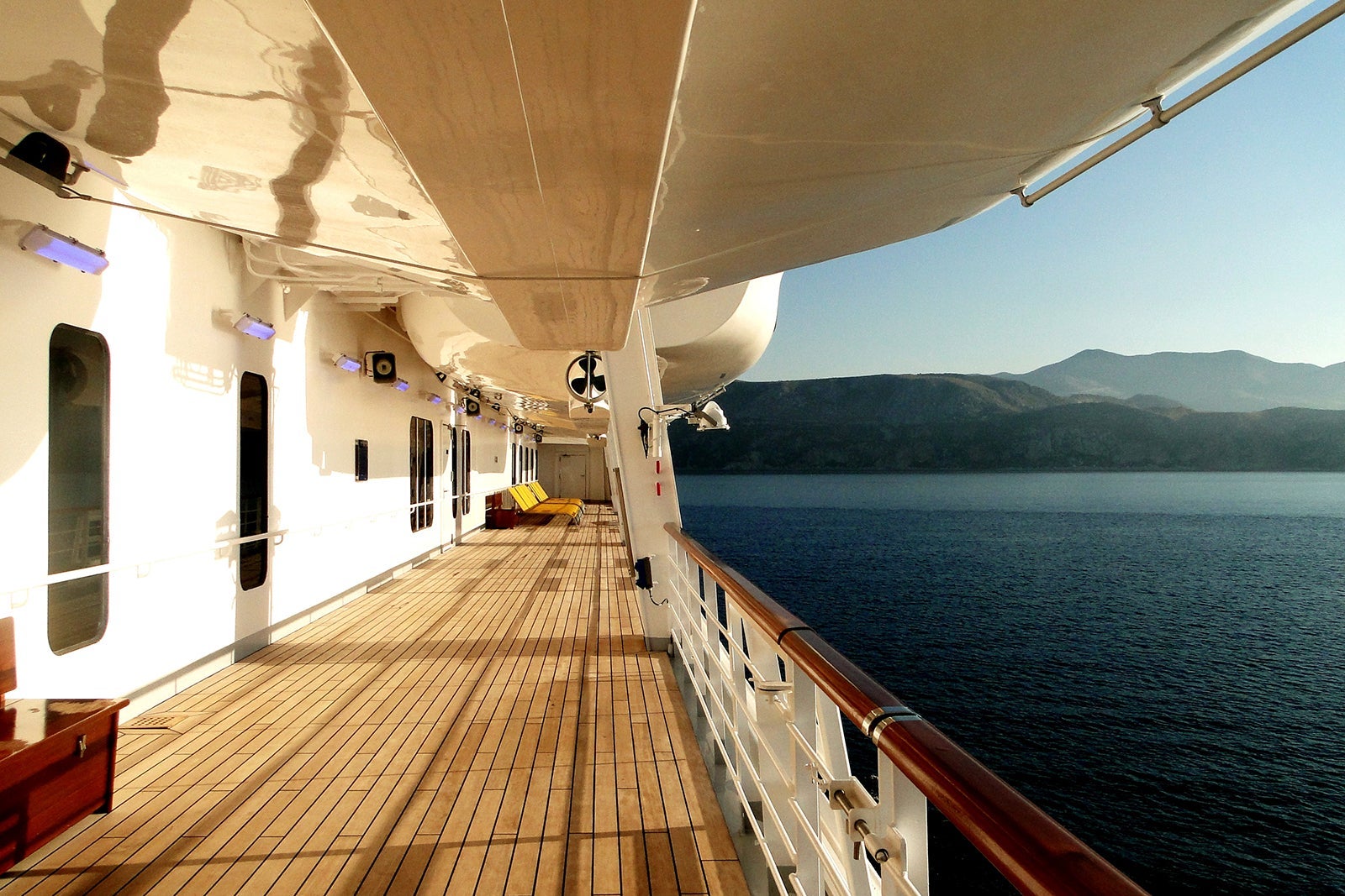 A view from the exterior promenade deck of a cruise ship showing teak decking and the water