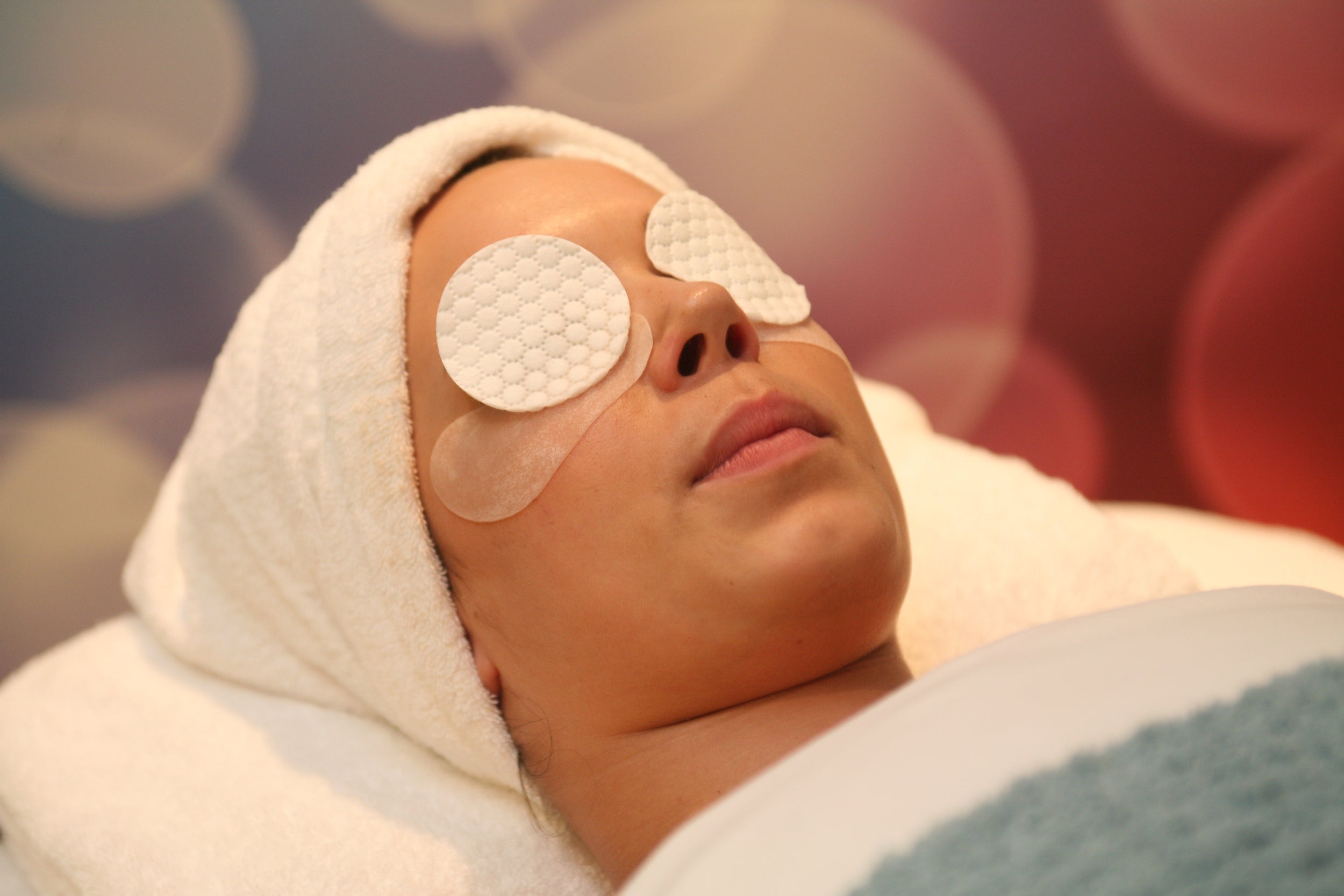 Woman lying down with a towel on her head and cotton pads on her eyes while receiving a spa treatment