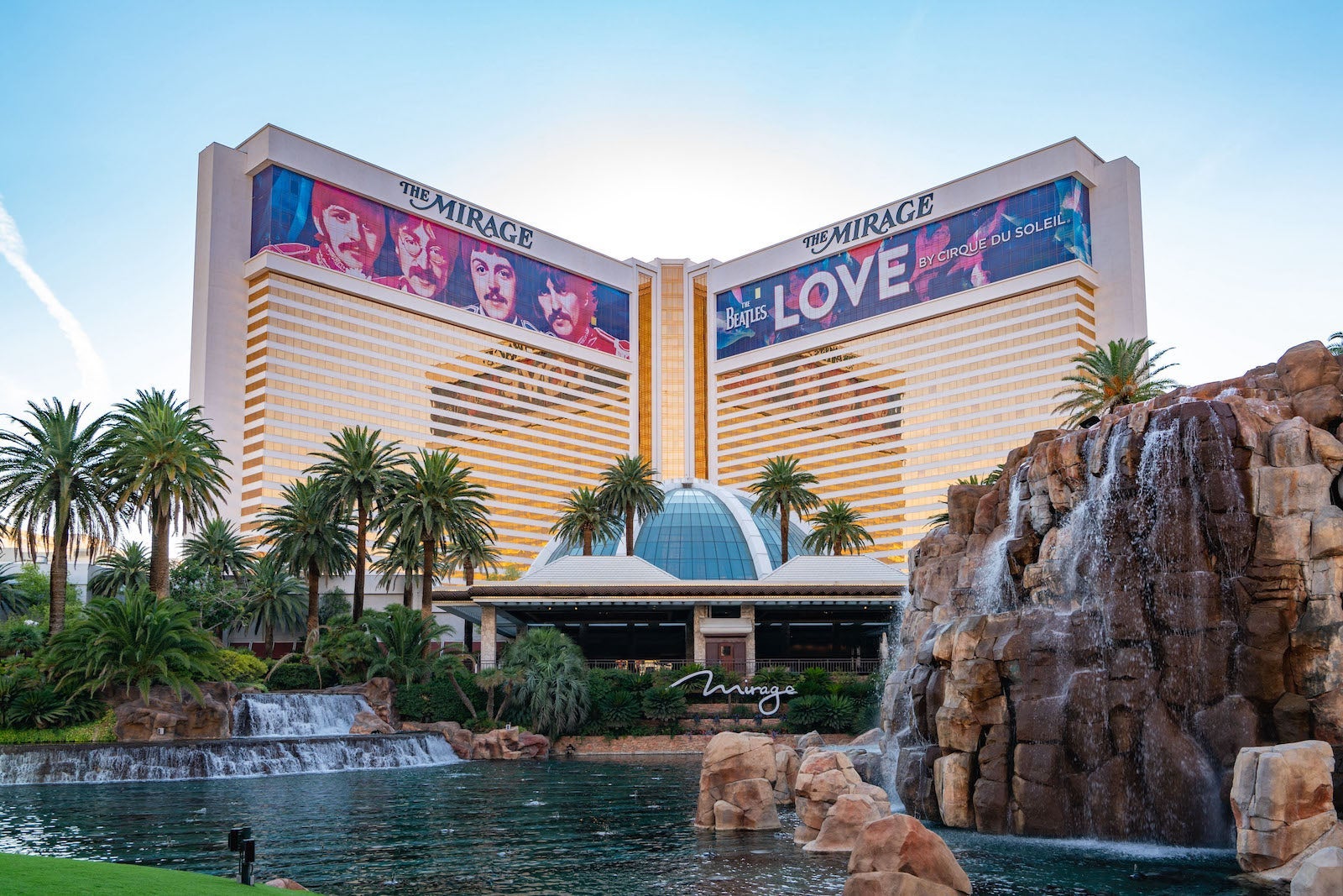 large gold and white building with rocky waterfall, palm trees and glass dome