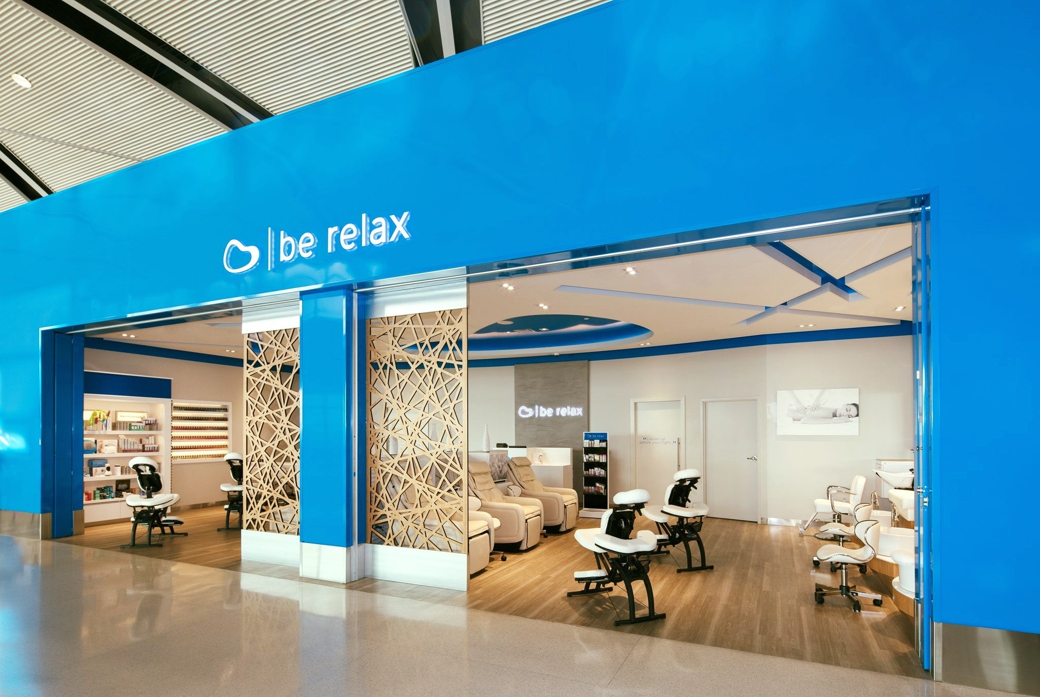massage chairs are visible inside a Be Relax location, seen from an airport hallway