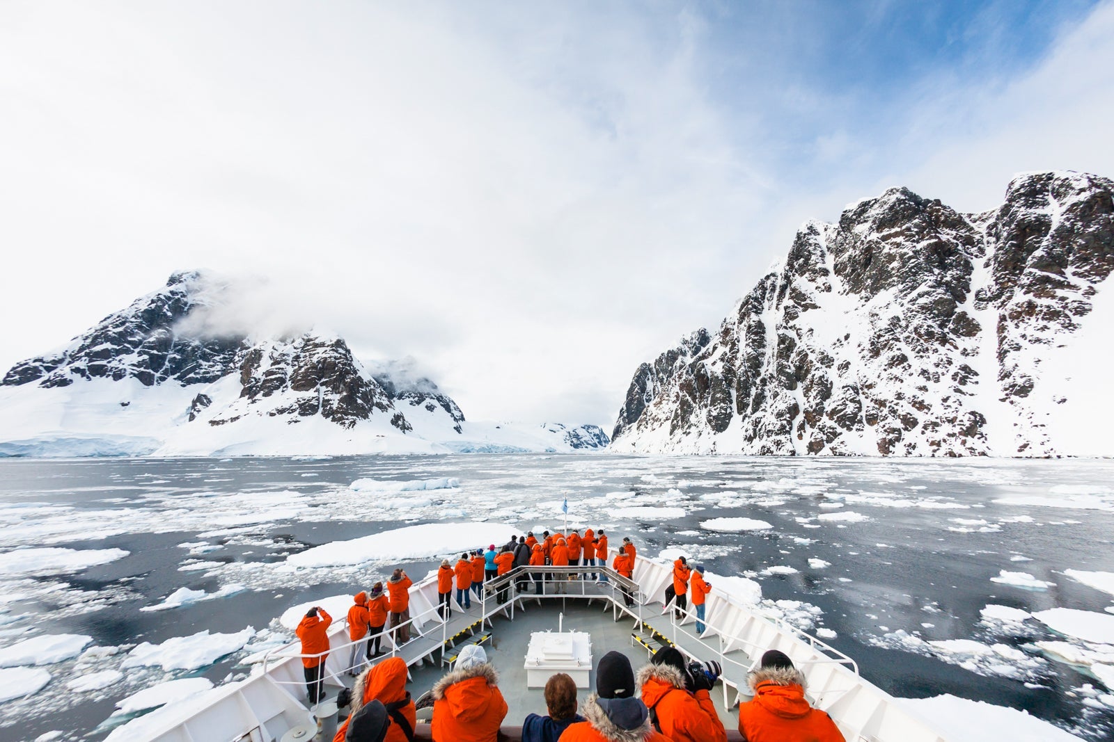 A cruise ship approaches the Lemaire Channel in Antarctica with red-coated passengers on deck
