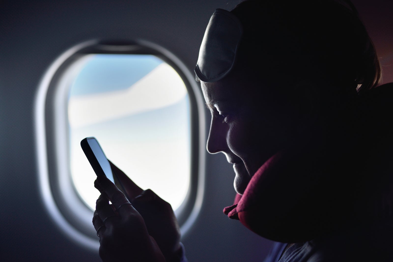 Airplane passenger wearing neck pillow checking phone