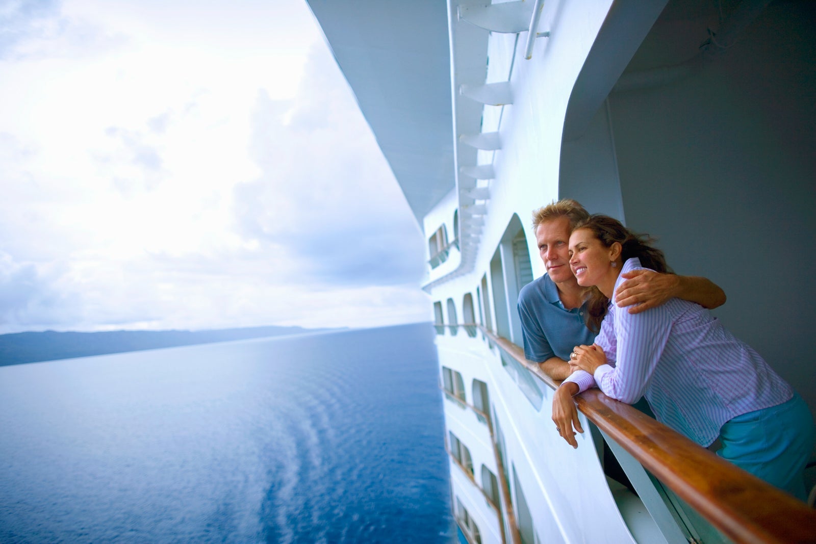 Couple leaning on cruise ship balcony railing while ship is at sea