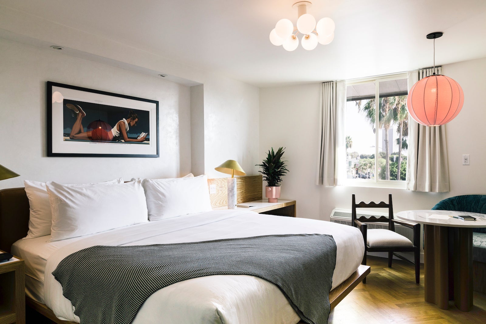 large hotel room with king bed, table, large picture, and pink hanging lamps