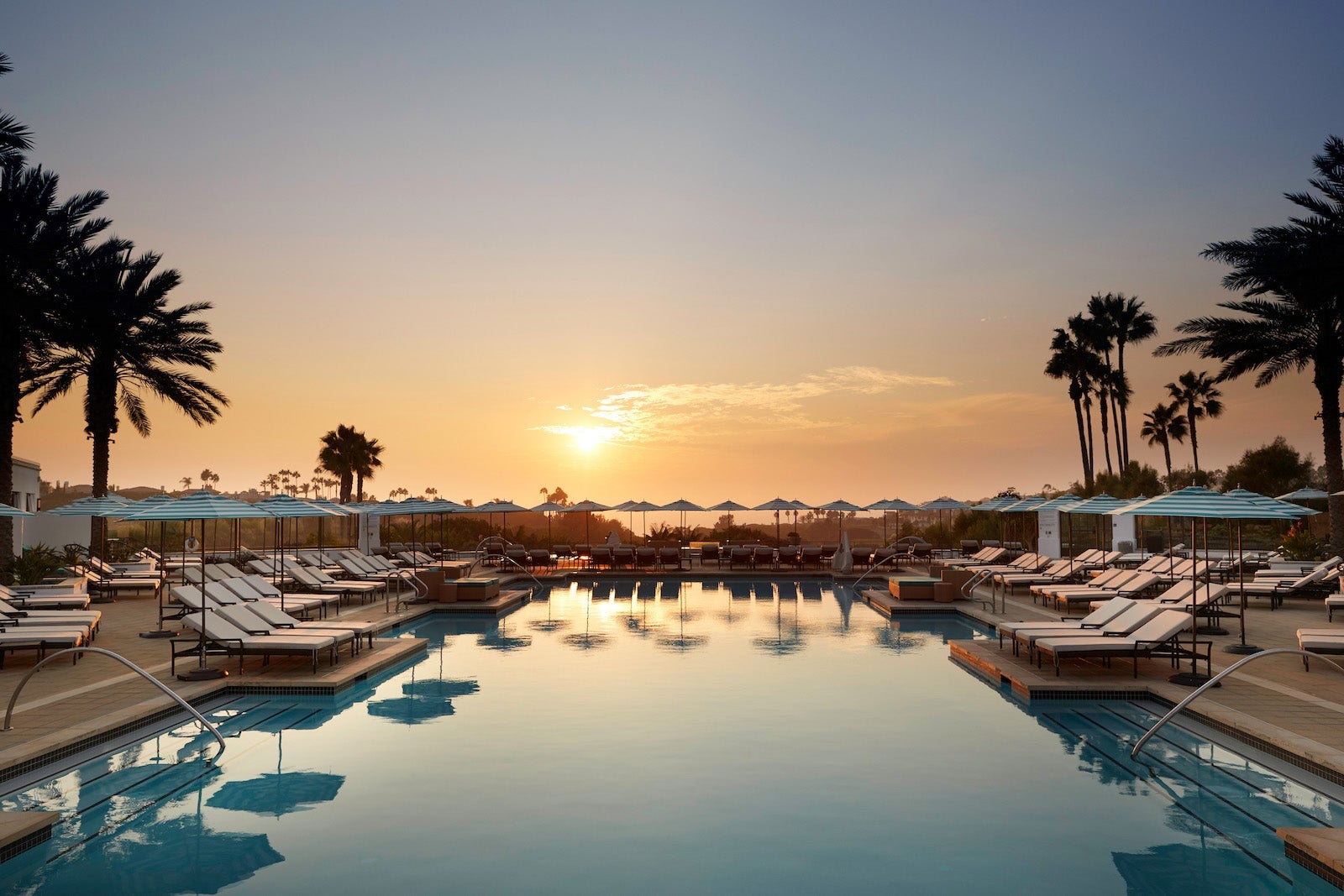 view of swimming pool with beach chairs and palm trees during sunset