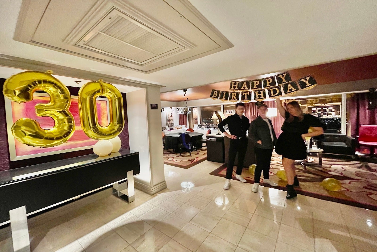 three friend posing with birthday banner in large hotel suite