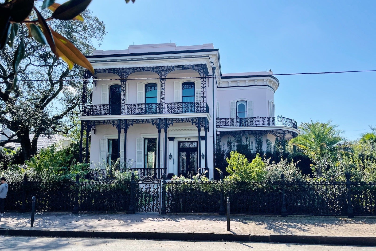 large white house with metal balcony surrounded by plants