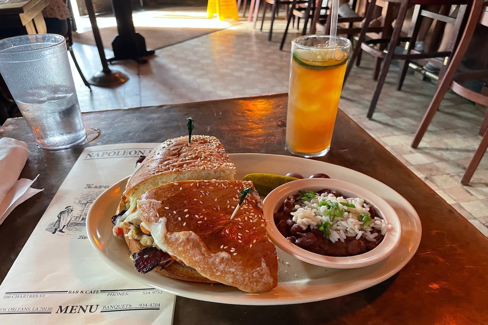 sandwich on plate with red beans rice, tall glass with liquor