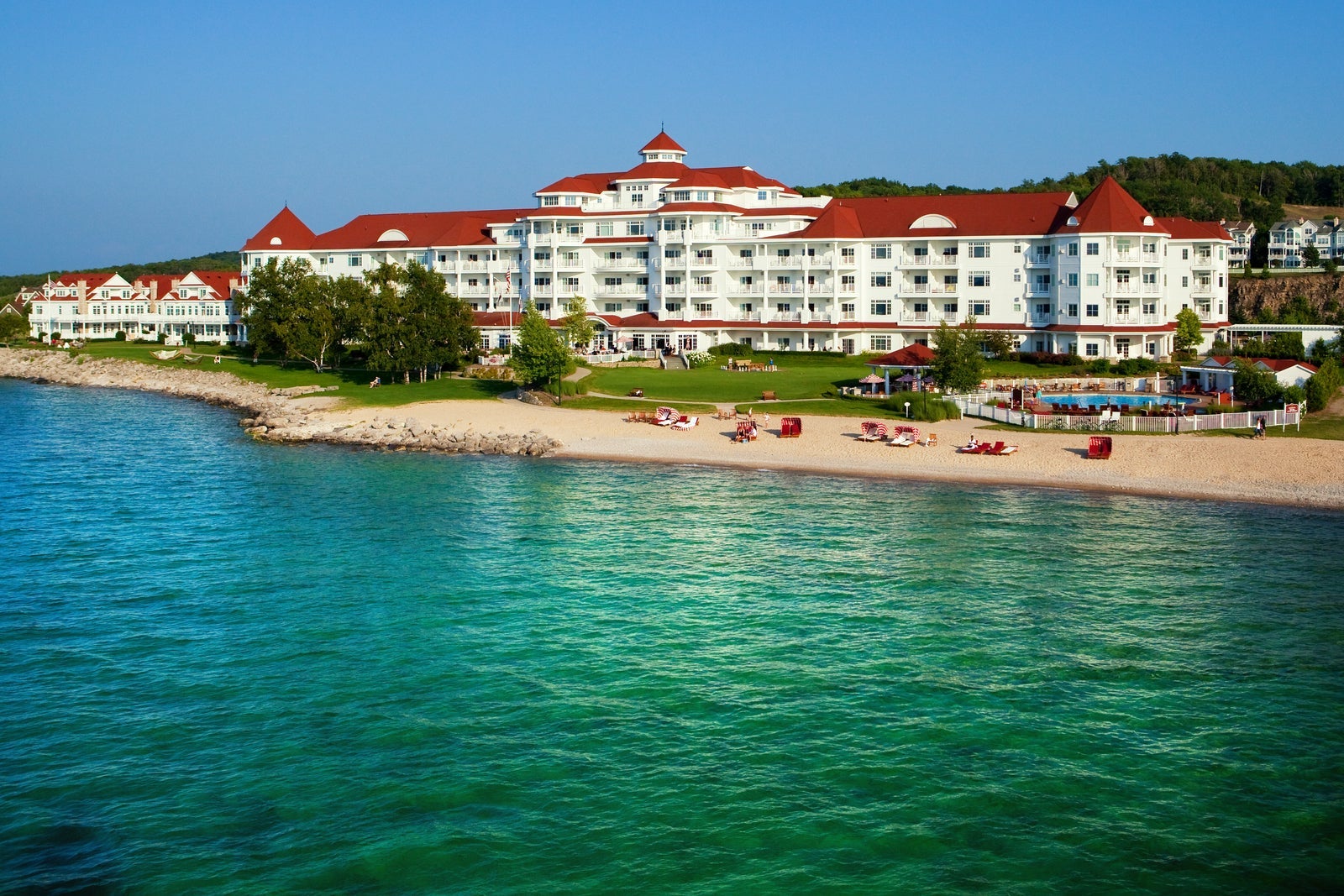 shot of large white hotel with red roof sitting on beach with blue-green water
