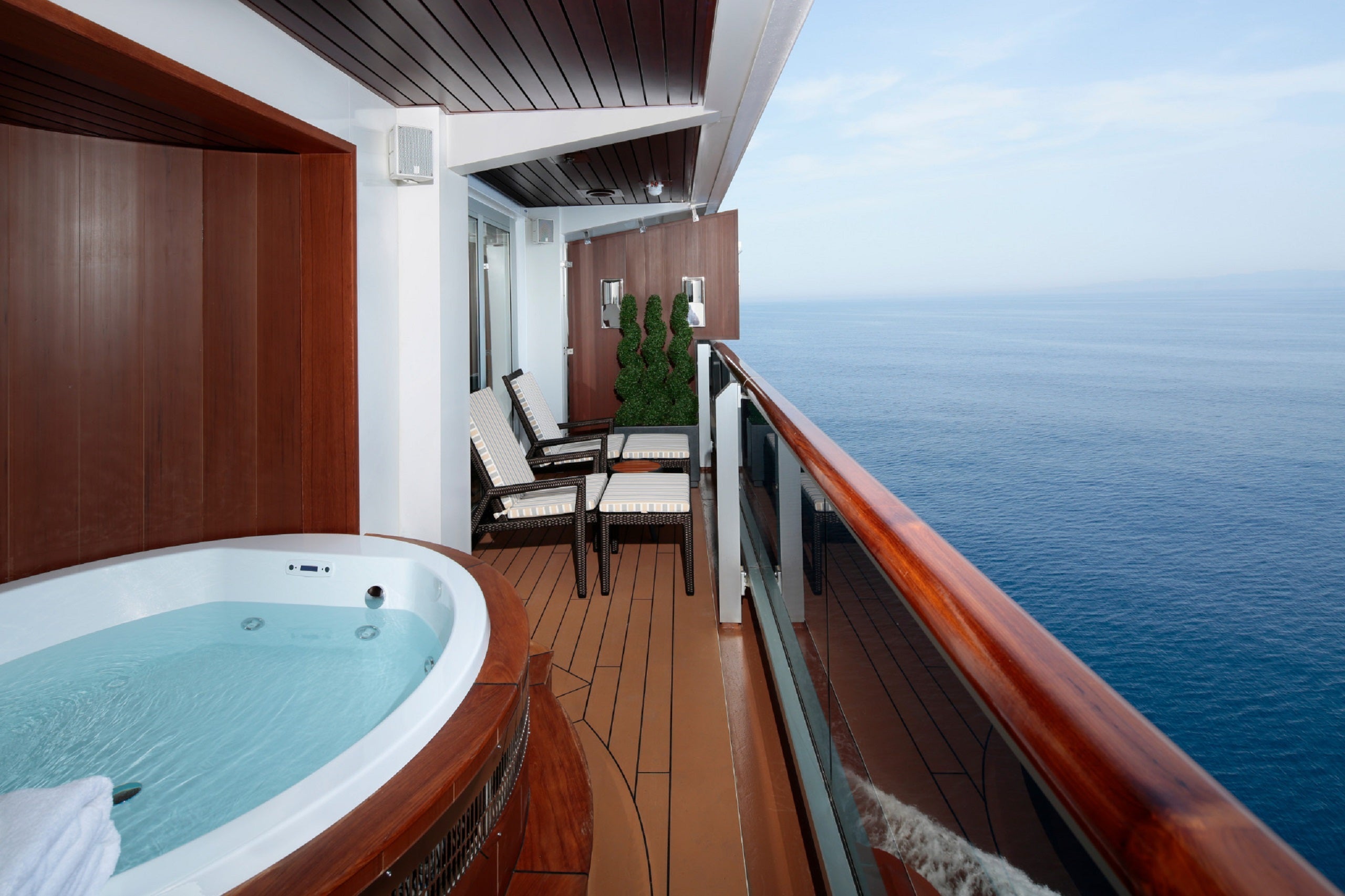 A large cruise suite balcony with a sitting area and a hot tub