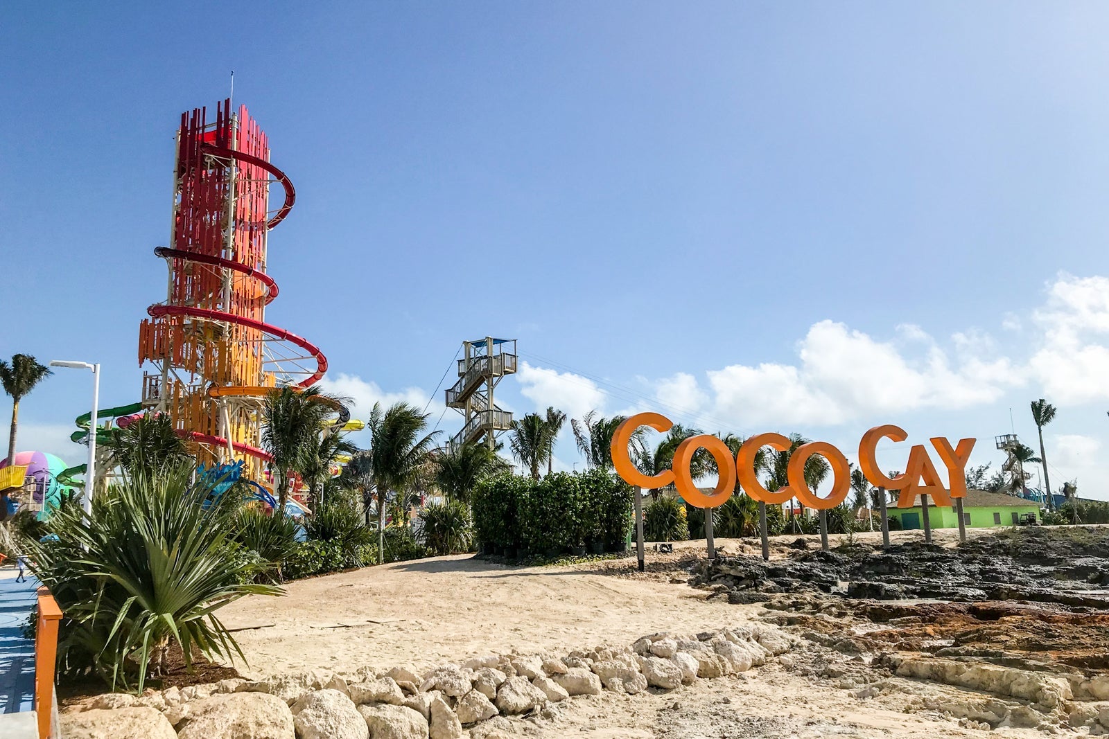 A large spiral waterslide rises up into blue sky on an island with a large orange sign reading "CocoCay"