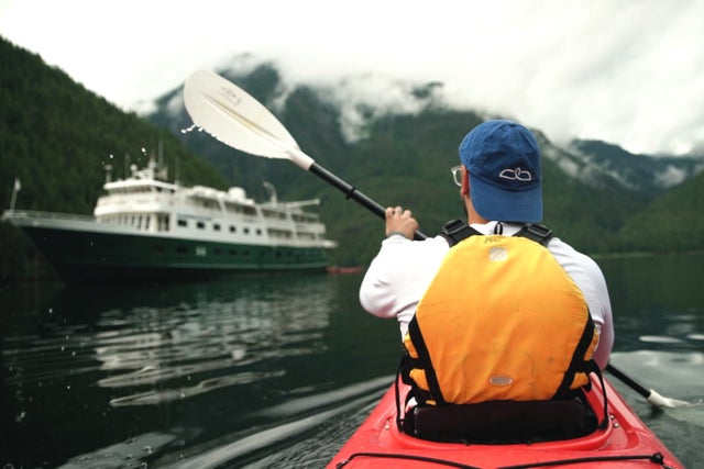 Man in baseball hat kayaking in Alaska's Misty Fjords near expedition cruise ship