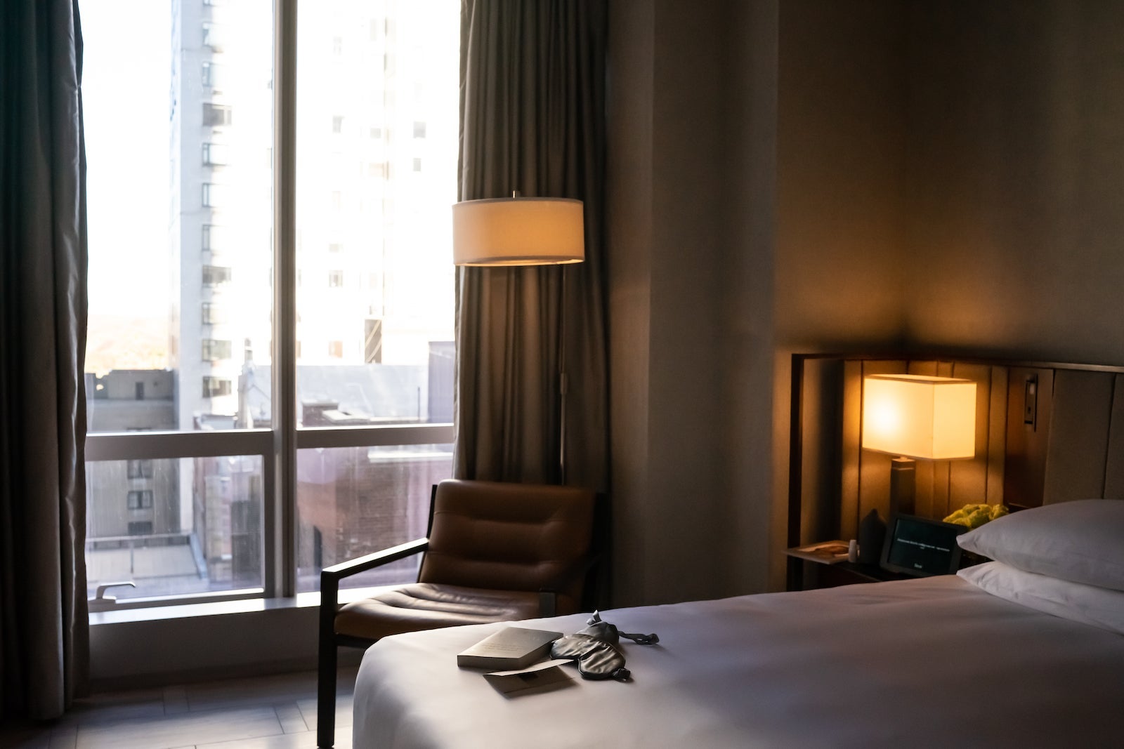 hotel room with bed, chair and window looking out at city