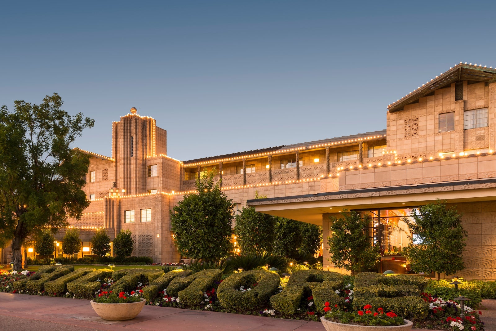 exterior of large hotel light up with lights and surrounded by bushes and tress