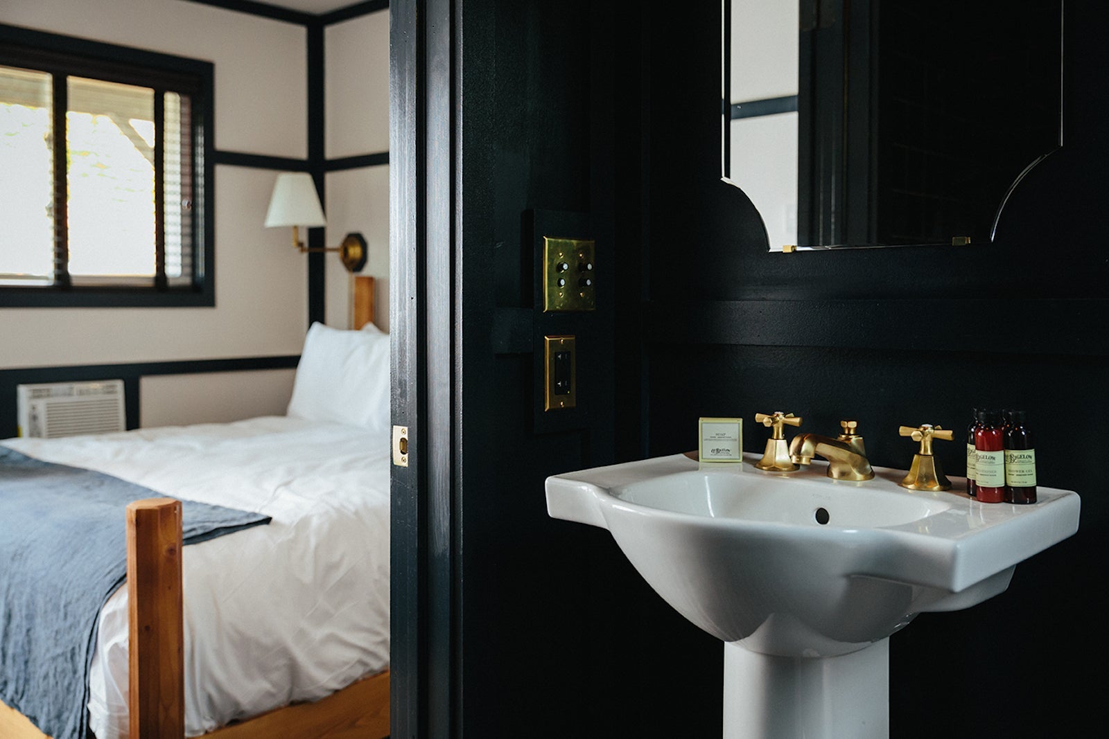 dark hotel bathroom with white sink and black walls looking into hotel room