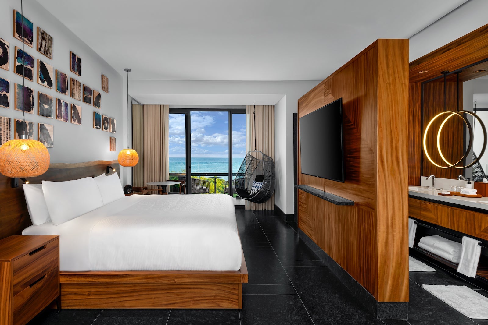 hotel room with wooden features, large white bed, hanging chair, bathroom and ocean views