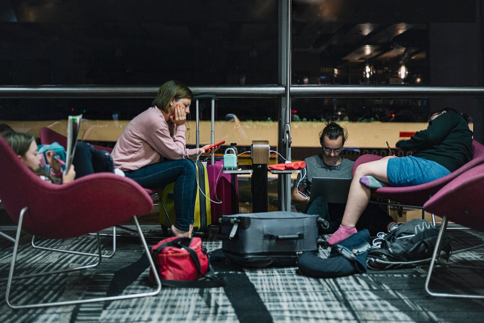 group of travelers sitting in chairs and on floor looking at their phones in distress