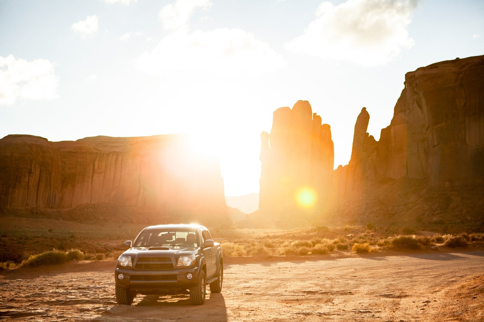 Off-road vehicle parked against rock formations at Monument Valley during sunny day
