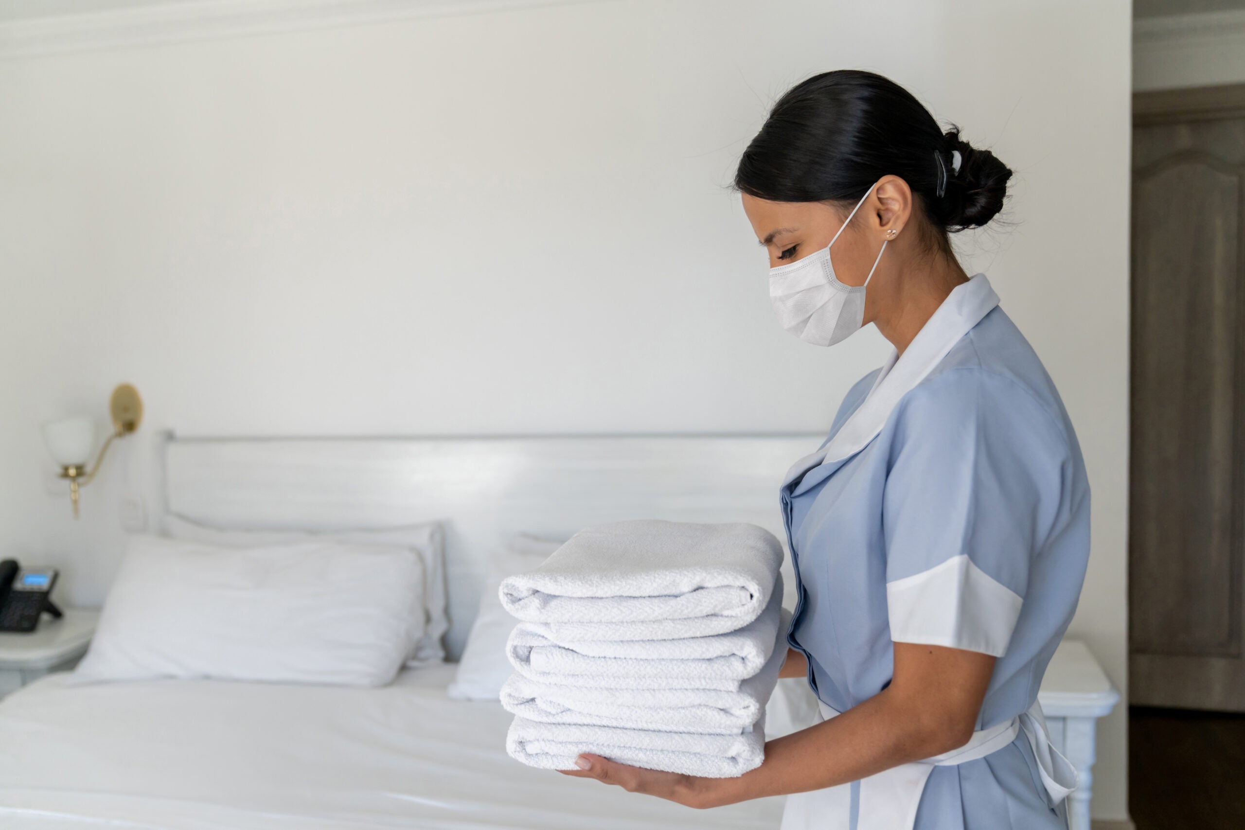 Housekeeper working at a hotel wearing a facemask and changing the towels. (Photo by Andresr/Getty Images)