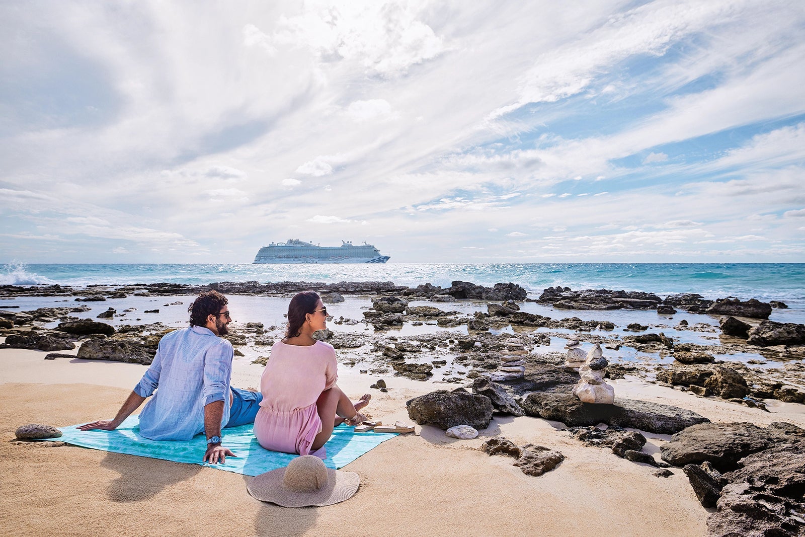 Couple sitting on rocky beach gazing out at Princess cruise ship