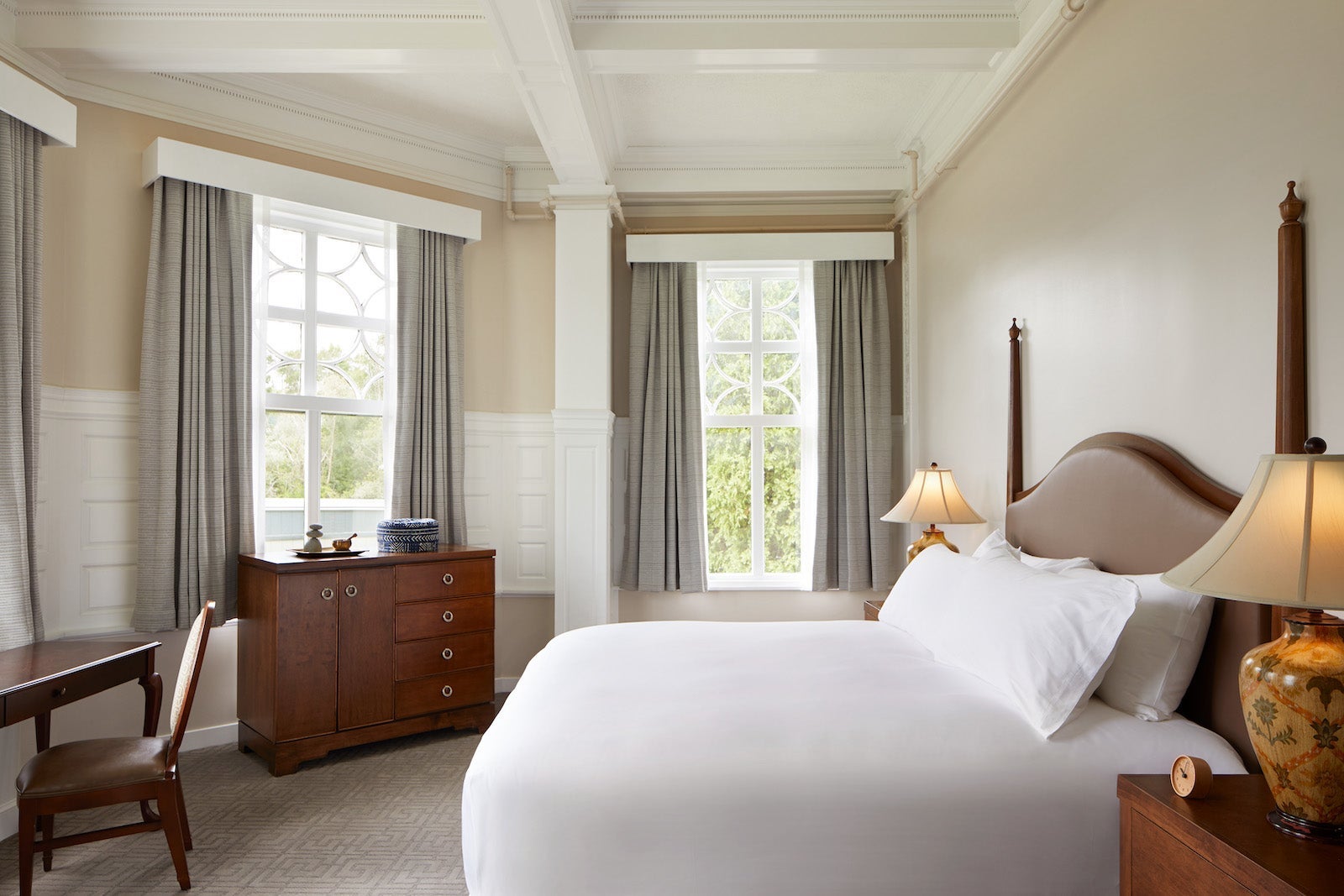 hotel room with large bed, white sheets, desk with chair and windows